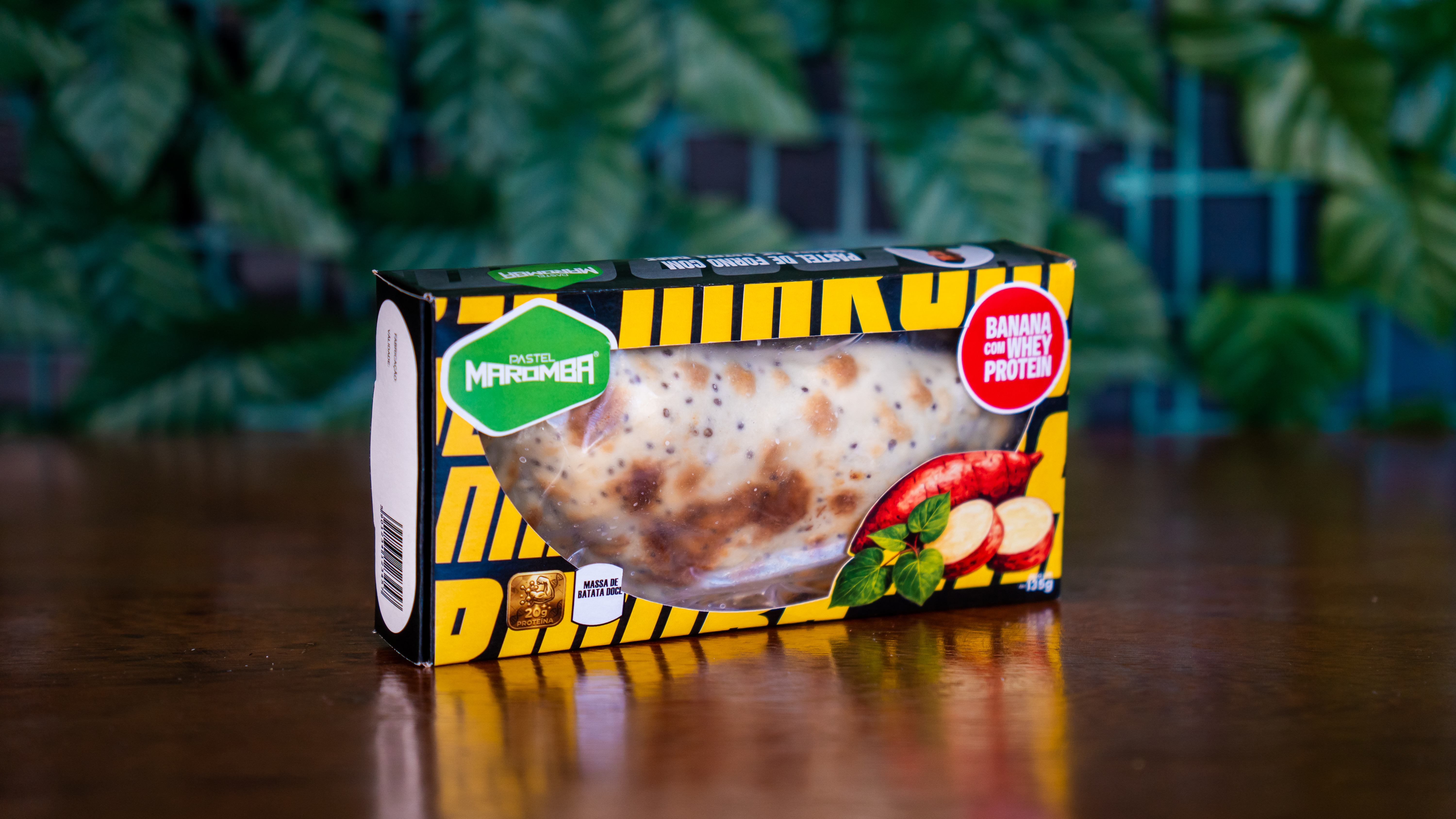 Caixa amarela de Pastel Maromba com selo Banana com Whey Protein sobre mesa de madeira