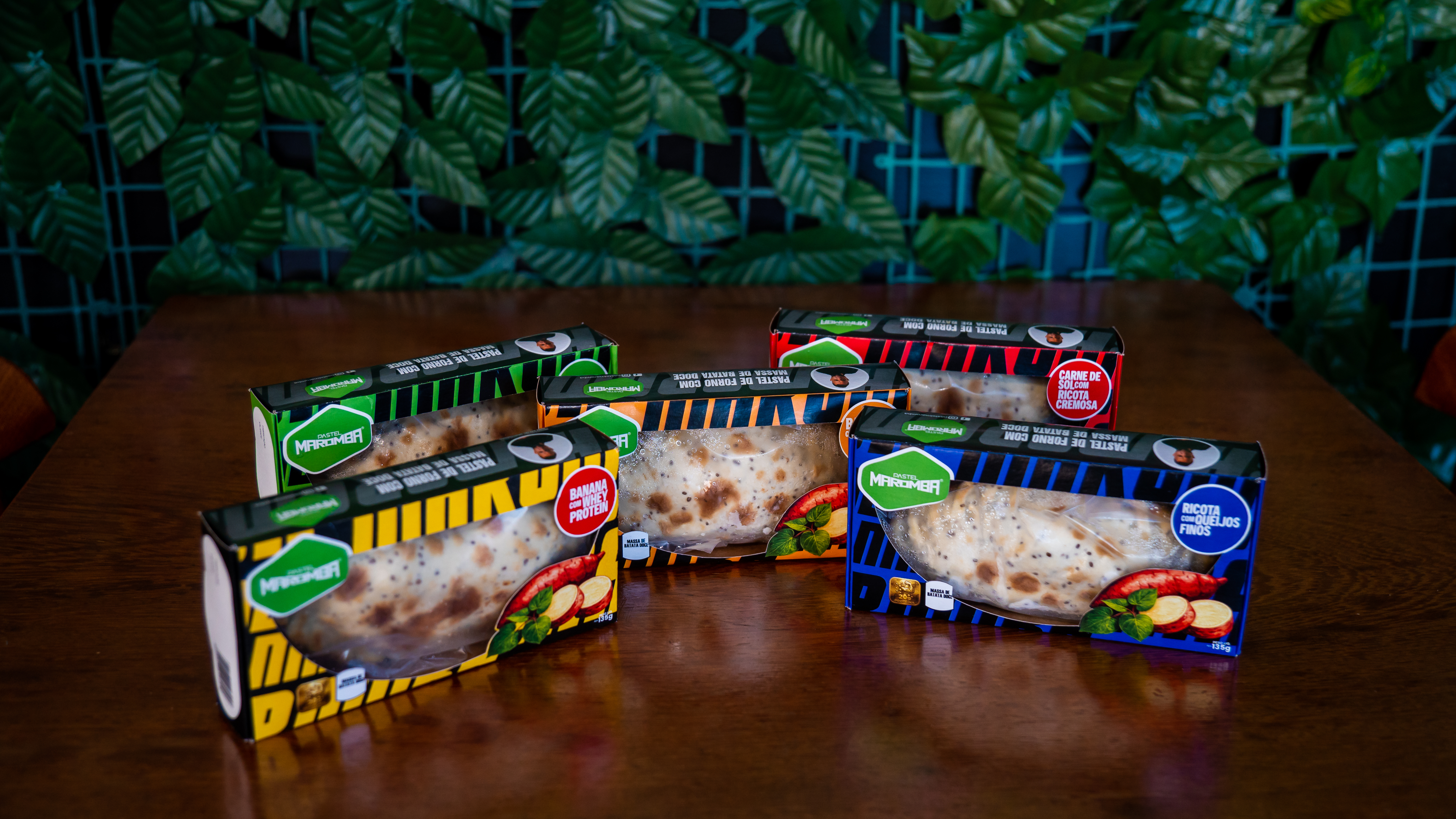 Cinco caixas de Pastel Maromba em cores diferentes dispostas sobre uma mesa de madeira
